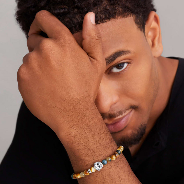 A man is wearing a sterling silver bracelet featuring a Tigereye gemstone beaded bracelet with a silver Caviar skull.