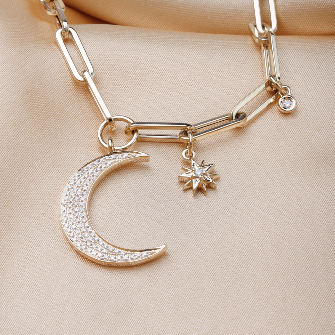 A close-up of a yellow-gold Moon and Stars Paperclip Chain against a gold background. The necklace features a moon-shaped pendant, 2 round diamonds, and a yellow-gold paperclip chain.