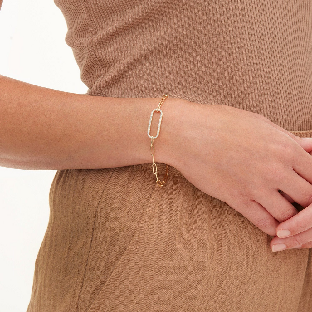 A close-up of a woman wearing a yellow-gold bracelet. The bracelet features a pave link focal element with a pave set of round diamonds and a paperclip link cable chain.