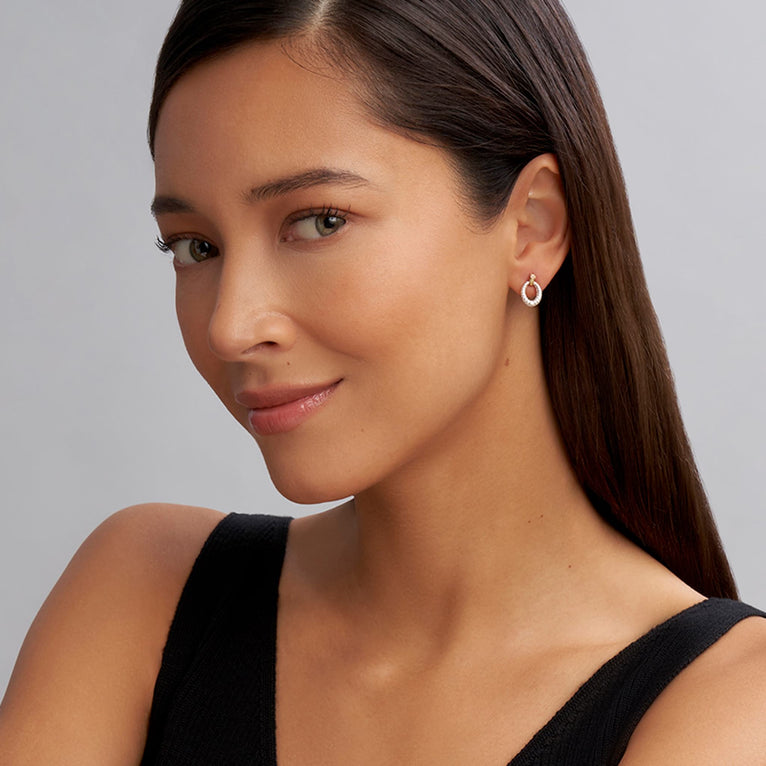 A woman wearing a black top and a pair of drop earrings with oval drop highlighted by 18k gold Caviar beading. 