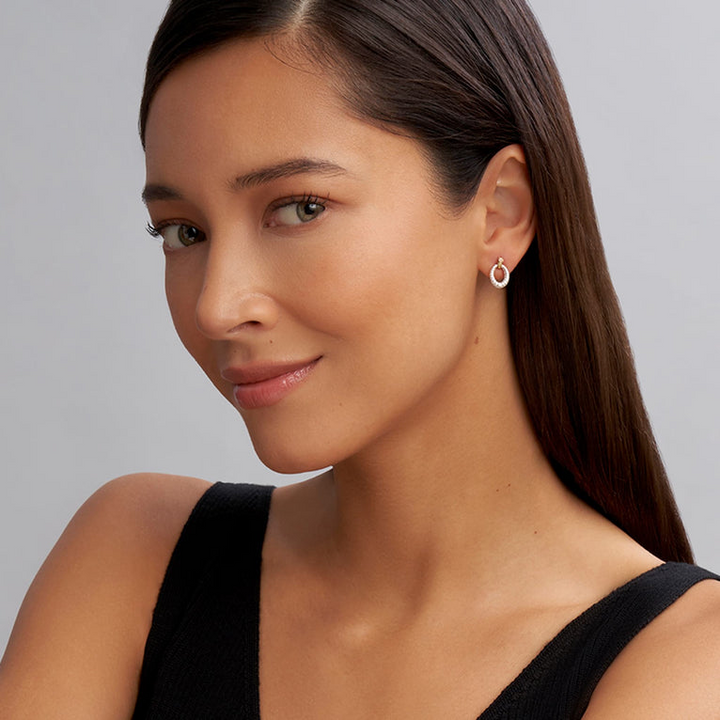 A woman wearing a black top and a pair of drop earrings with oval drop highlighted by 18k gold Caviar beading. 