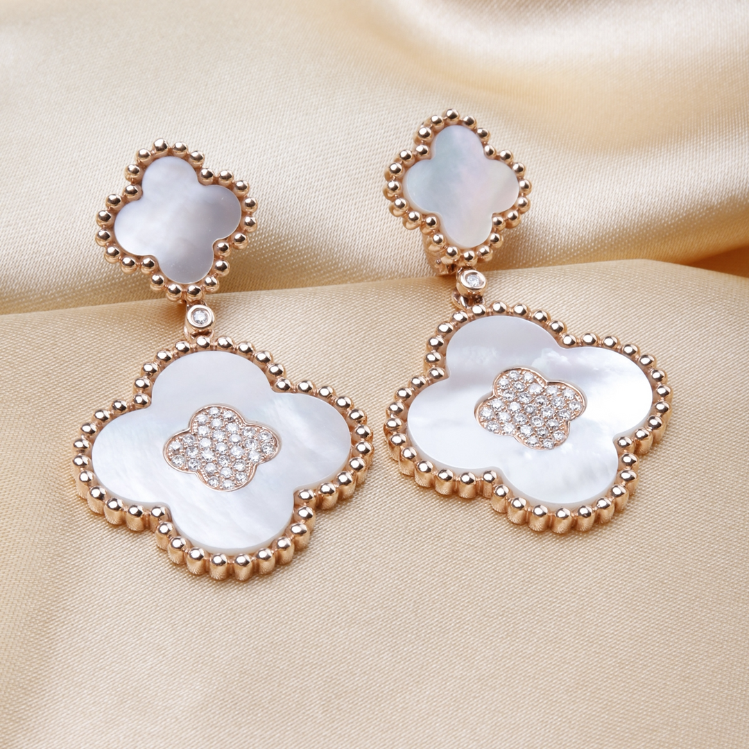 A pair of drop earrings with two clover motifs with white mother-of-pearl stones and gold caviar beading lied against a gold background.