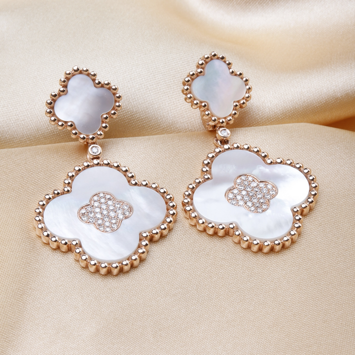 A pair of drop earrings with two clover motifs with white mother-of-pearl stones and gold caviar beading lied against a gold background.