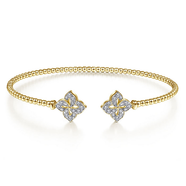 A yellow gold cuff bracelet is in the middle of a white background. The bracelet features a beaded band and hibicuius diamond-set motif endcaps.