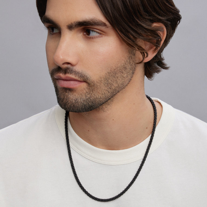 A man wearing a sterling silver and ceramic beaded necklace featuring matte black ceramic caviar beading.