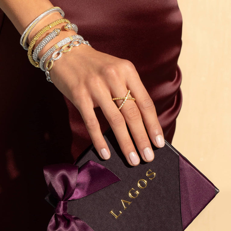 A close-up of a woman wearing a black top and a Sterling Silver & 18k gold bangle bracelet. The bracelet has caviar beading with an X design.