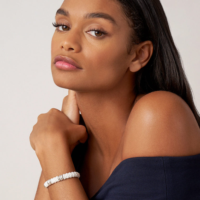 A woman wearing a sterling silver bracelet, featuring three diamond stations, white ceramic caviar beading, and sterling silver stations