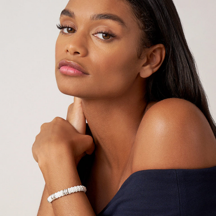 A woman wearing a sterling silver bracelet, featuring three diamond stations, white ceramic caviar beading, and sterling silver stations