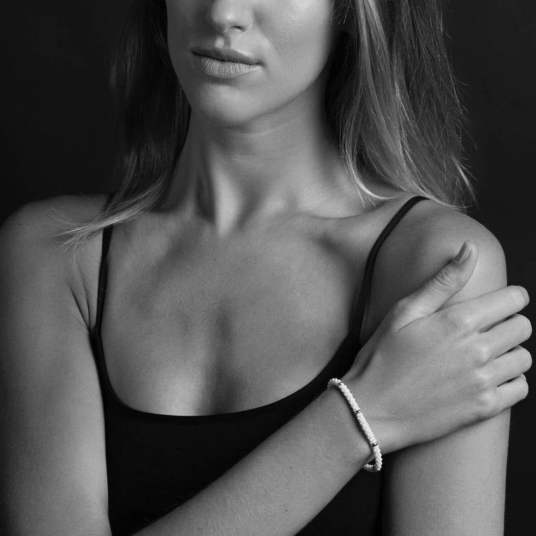 A woman wearing a Sterling silver and 18k gold bracelet featuring five sterling silver stations and white ceramic caviar beading.