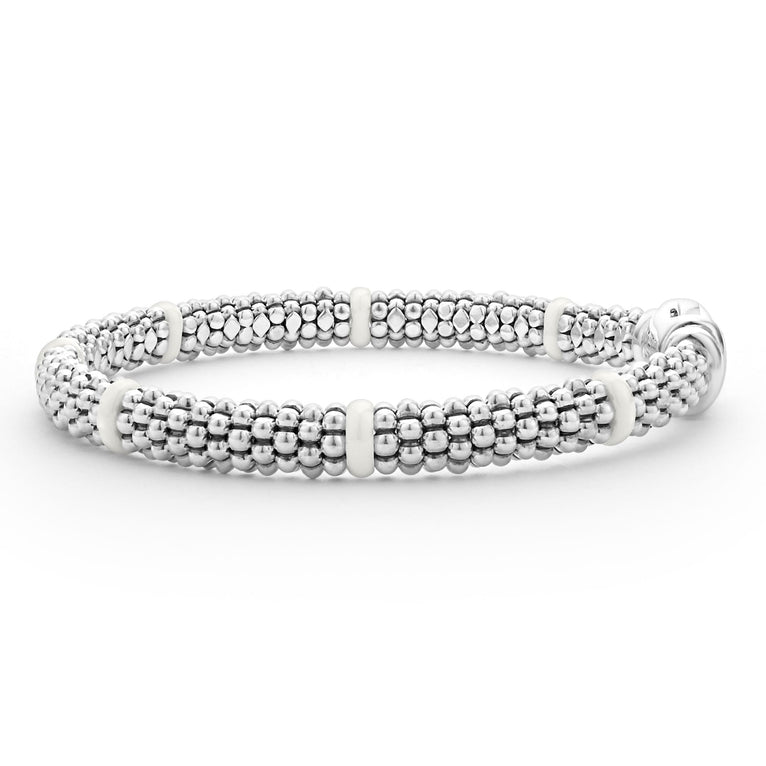 A side-view of a sterling silver and ceramic beaded bracelet in the middle of a white background featuring seven smooth white ceramic stations and silver Caviar beading.