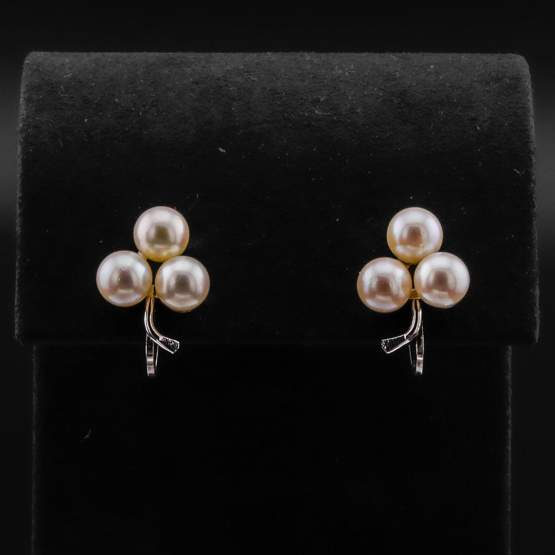 A pair of stud earrings with pearls arranged in a cluster design against a black background.