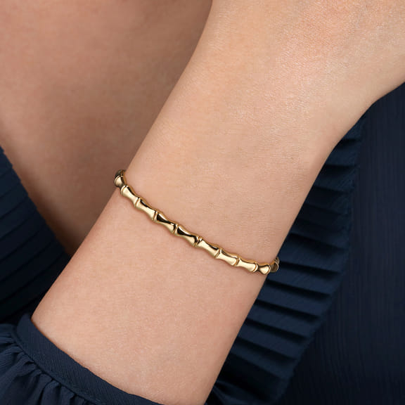 Model wearing the Gabriel & Co yellow gold bamboo-style bangle with a navy blouse
