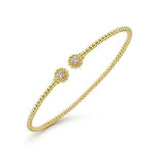 A yellow-gold bangle bracelet with a beaded band and sunflower bujukan cuff end caps is angled in the middle of a white background.