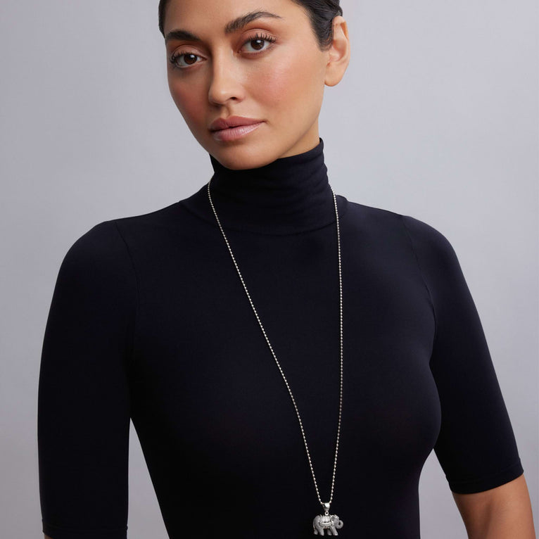 A woman is wearing a sterling silver necklace in the middle of the white background featuring a elephant pendant on a ball chain