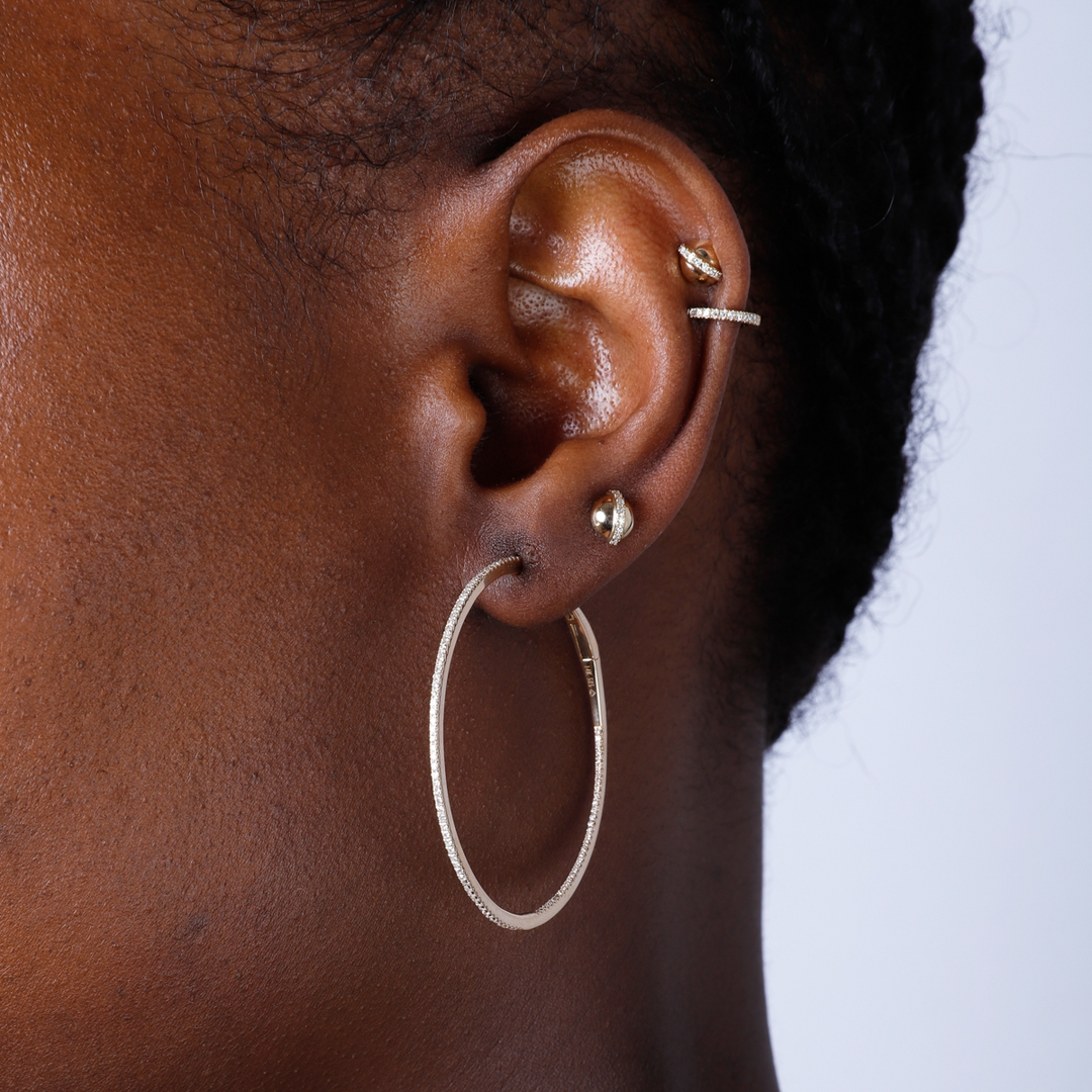 A woman is wearing a pair of yellow-gold hoop earrings with a single row of round diamonds. 