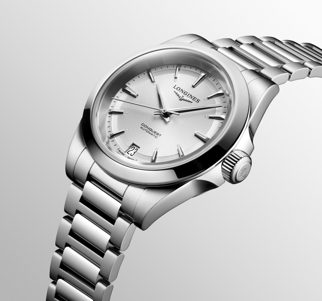 A Longines watch is displayed in the middle angled to the right on a white background. The watch features a silver dial, silver hands and markers, a stainless steel bezel, and a stainless steel bracelet.