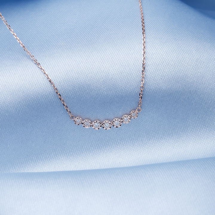 A close-up of a yellow-gold Cosmic Crescent Diamond Necklace against a blue background. The necklace features a celestial-inspired pendant set with diamonds.