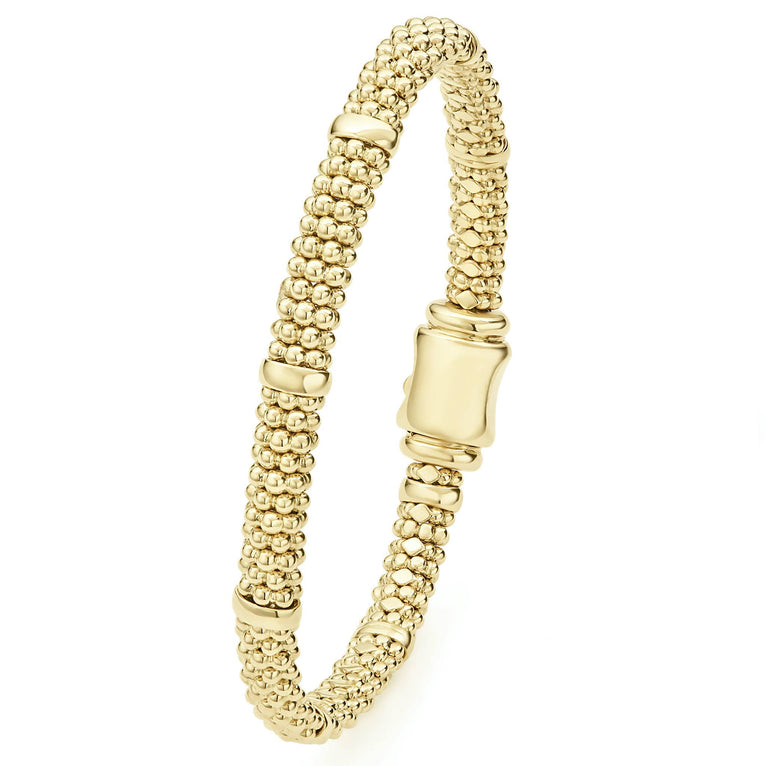 An 18k gold bracelet is angled to the side in the middle of a white background. The bracelet features smooth stations and caviar beading.