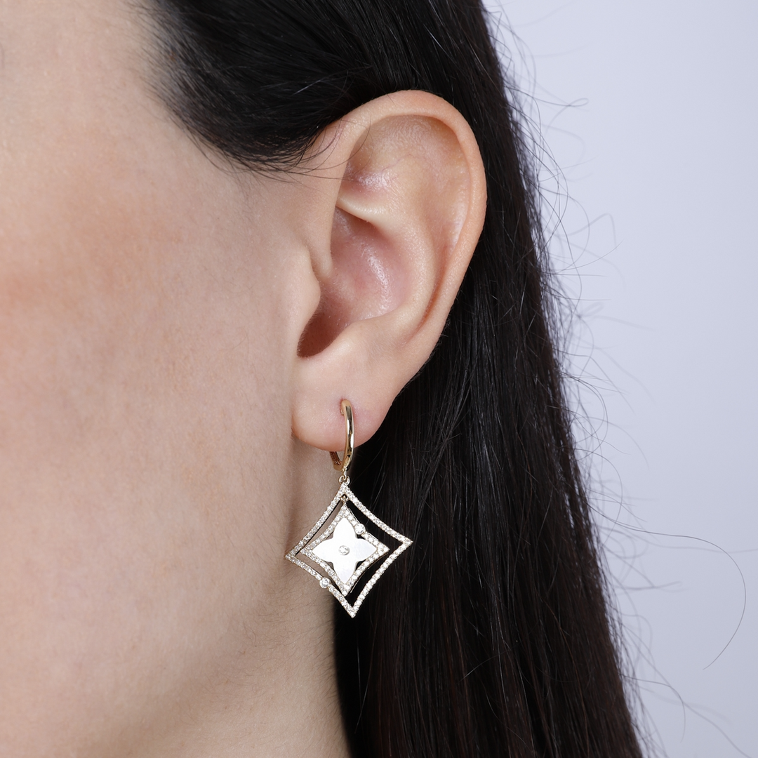 A woman with long black hair is wearing a pair of drop earrings with a mother-of-pearl Northstar motif and diamond-set halos. 