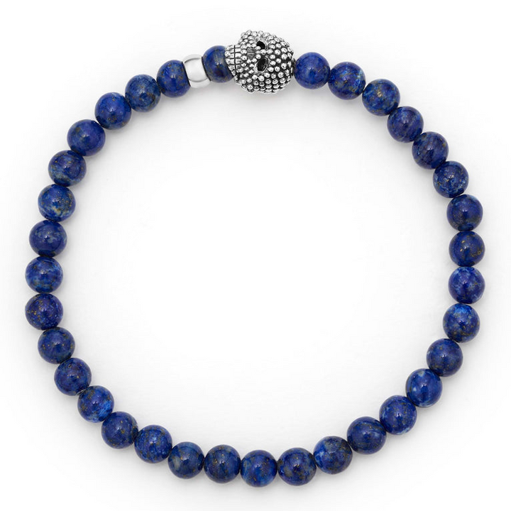 A sterling silver bracelet is displayed in the middle of a white background featuring a Lapis gemstone beaded bracelet with a sterling silver Caviar skull.