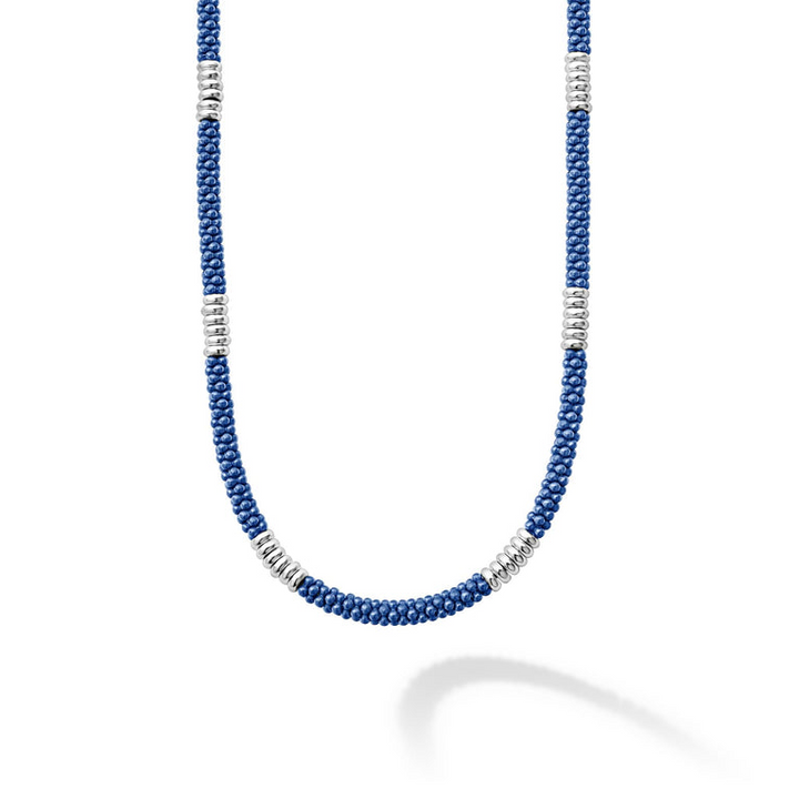 A close-up of a sterling silver and ceramic beaded necklace in the middle of a white background featuring blue ceramic and silver Caviar beading.