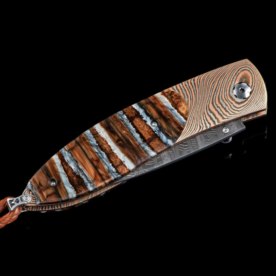 A close-up of a pocket knife with the blade in the case. The pocket knife features a twisted Mokume gane frame, inlaid 10,000-year-old fossil Woolly Mammoth tooth, and ‘Hornets Nest’ damascus steel blade.