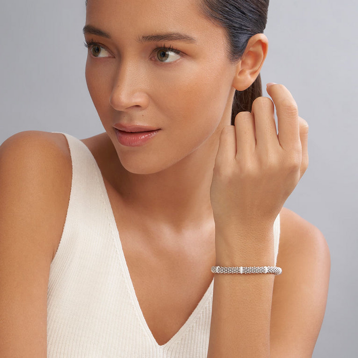 A woman is wearing a sterling silver and ceramic beaded bracelet featuring seven smooth white ceramic stations and silver Caviar beading.