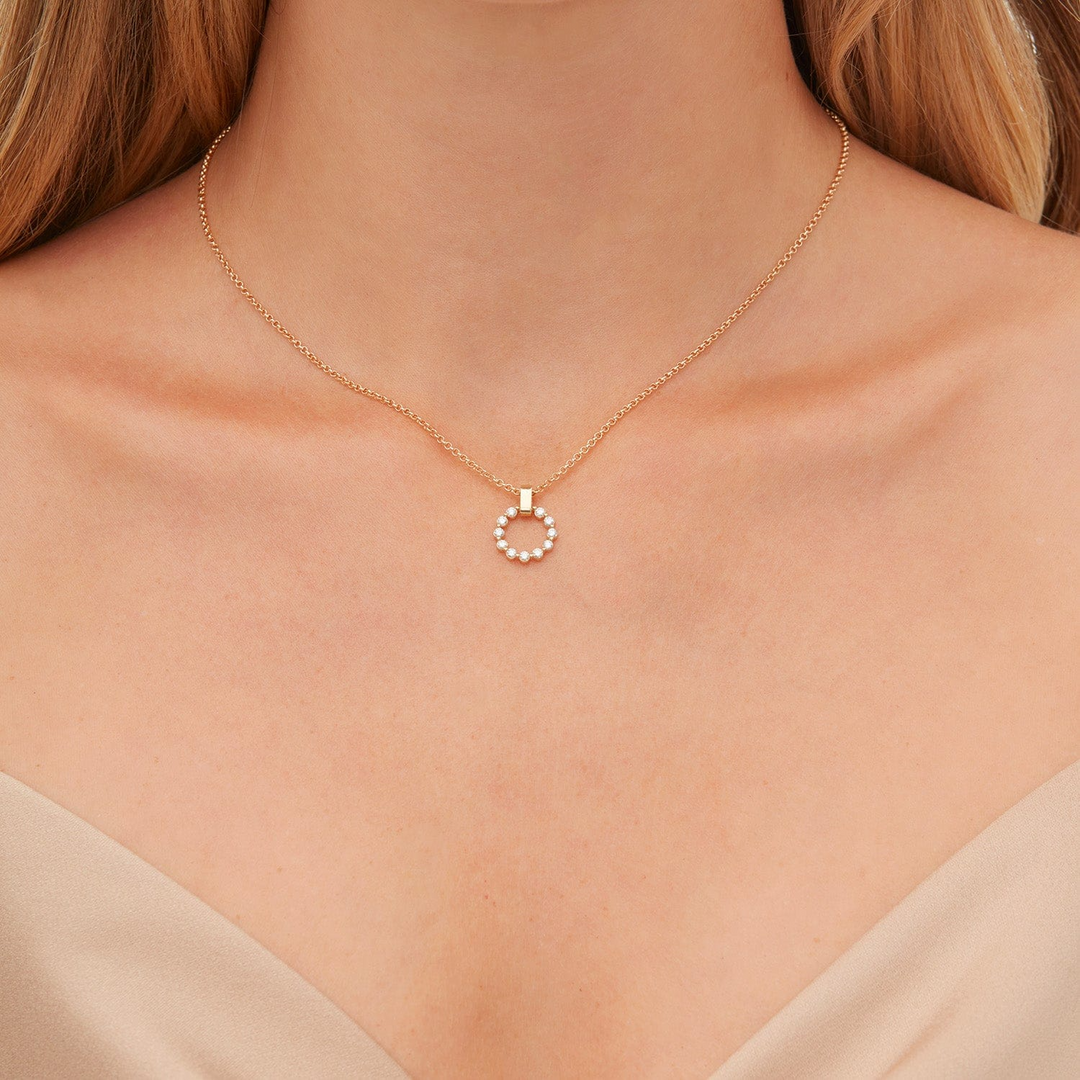 A close-up of a woman wearing a yellow-gold necklace. The bracelet features a circle pendant and a smooth gold bar with a belcher chain.