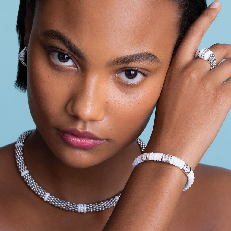 A woman is wearing a sterling silver and 18k gold necklace featuring white stations, one diamond set station, and caviar beading.