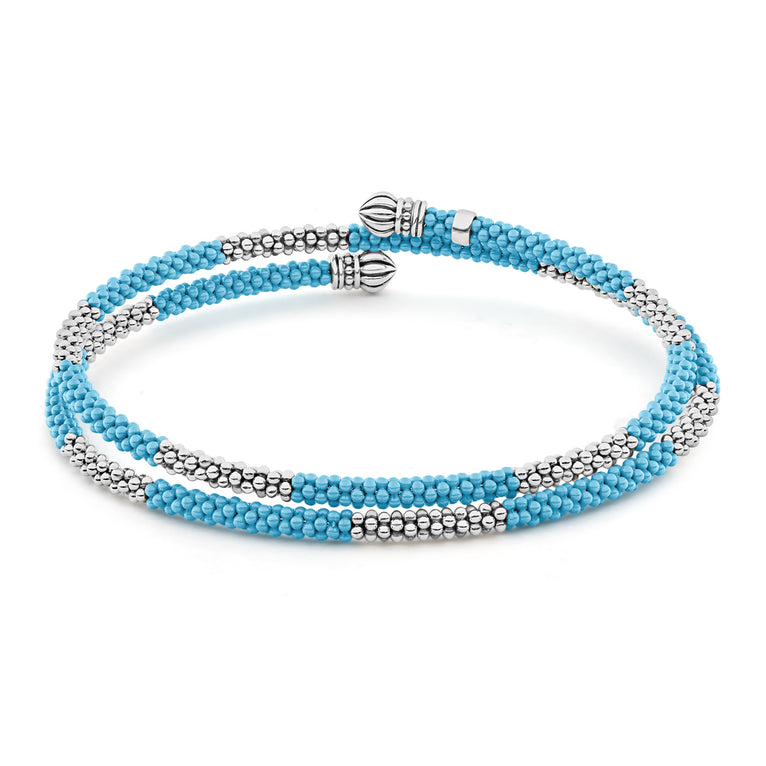 A sterling silver bracelet in the middle of a white background featuring ten sterling silver stations highlighted by blue ceramic Caviar beading finished with fluted sterling silver endcaps