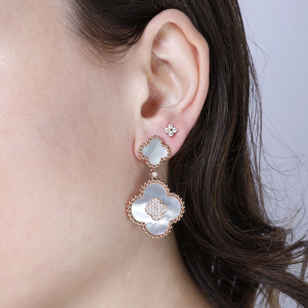 A woman with brunette hair wearing a pair of drop earrings with two clover motifs with white mother-of-pearl stones and gold caviar beading.