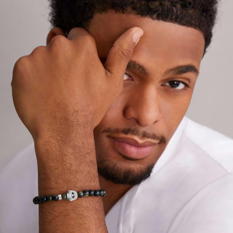 A man is wearing a sterling silver bracelet featuring a Golden Obsidian gemstone beaded bracelet with a silver Caviar skull.