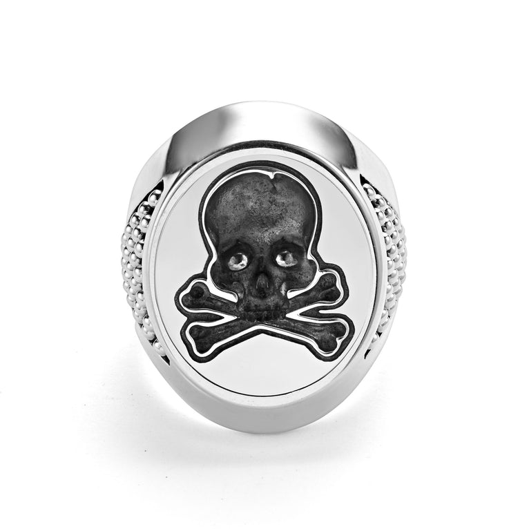 A sterling silver ring in the middle of a white background featuring a skull motif on the signet ring