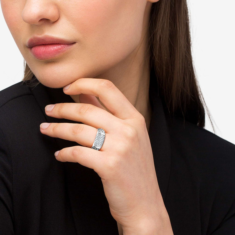A close-up of a woman with brown hair, wearing a black top and a white gold ring on her ring finger. The ring features Pavé diamonds and sterling silver Caviar beading with sterling silver stations in between the diamonds and beading.
