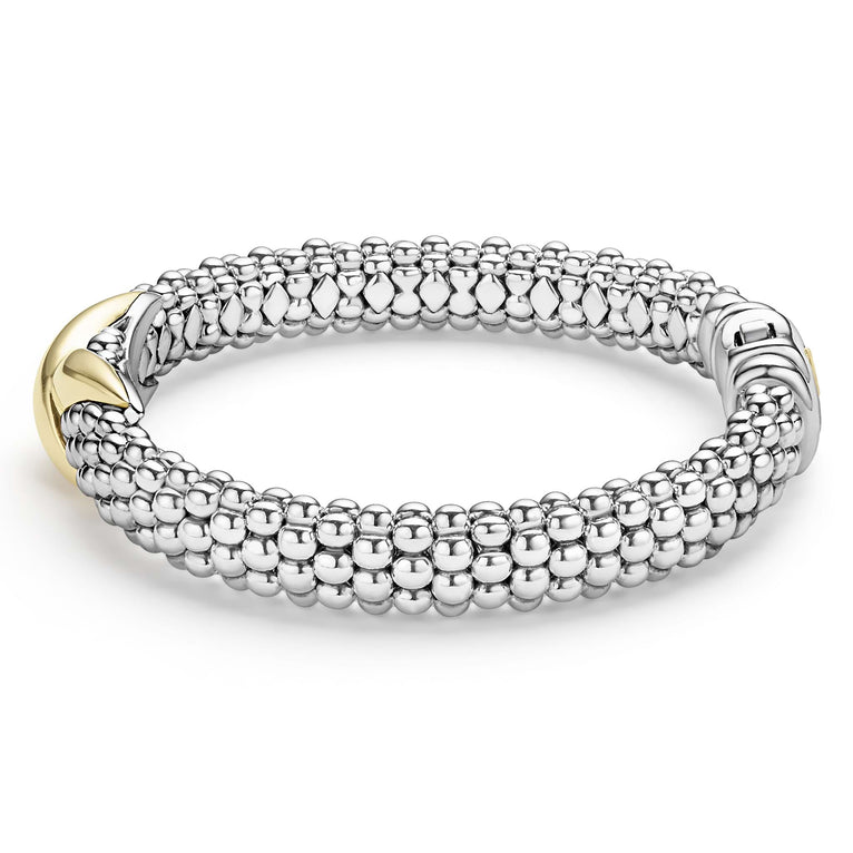 A side-view of a Sterling Silver & 18k gold bracelet in the middle of a white background. The bracelet features a gold X station, caviar beading, and a stainless steel clasp.