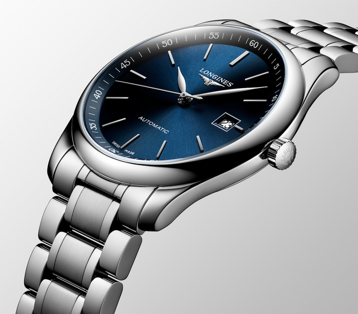 Close-up of a Longines watch, highlighting the right side profile and bracelet. The watch features a blue dial, silver hands and markers, a stainless steel bezel, a crown on the right side, and a stainless steel bracelet.