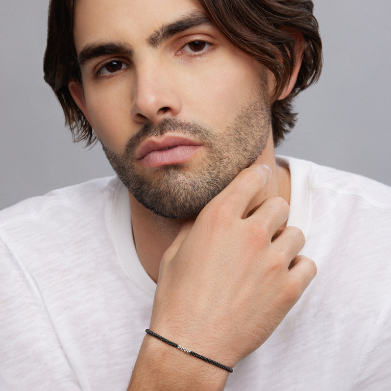 A man is wearing a bracelet featuring three sterling silver stations and Matte black ceramic caviar beading