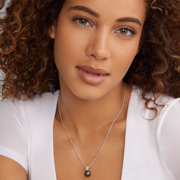 A close-up of a woman wearing a sterling silver & 18k gold necklace featuring a tahitian black pearl against a white background.