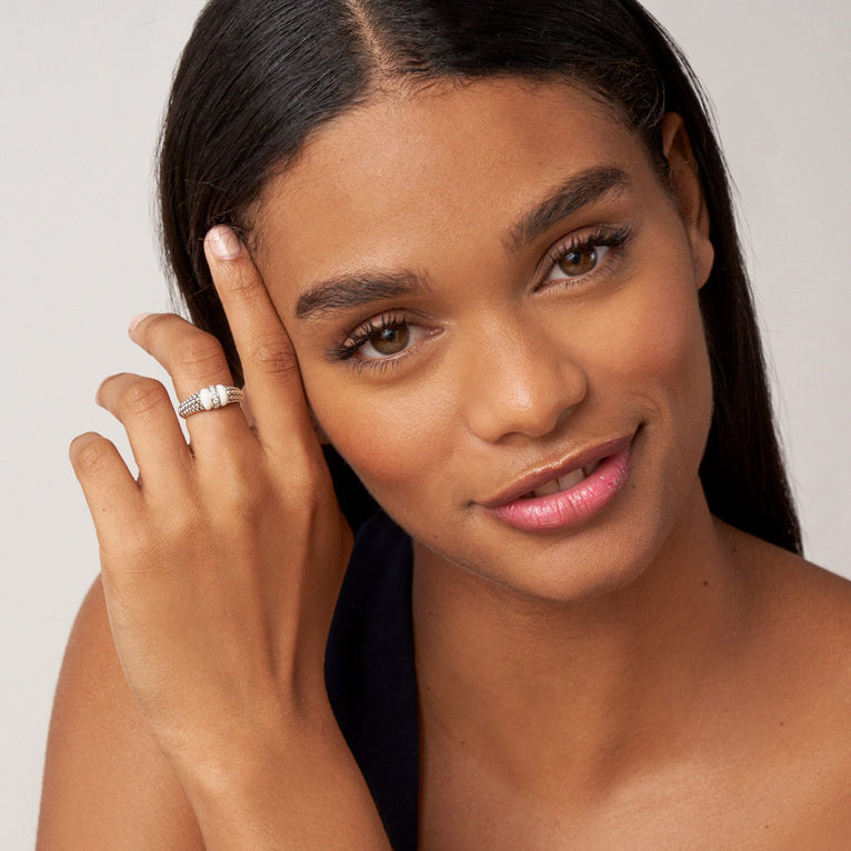 A woman rests her hand on her cheek, showcasing the ring on her middle finger. The ring features a white gold caviar beaded band, two white bar stations, and a single diamond-set row station.