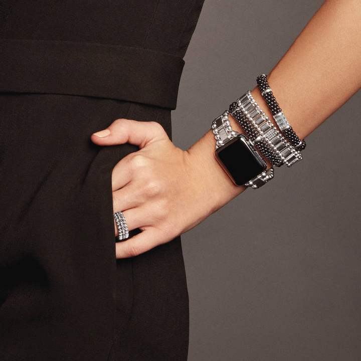 A woman wearing a sterling silver bracelet, featuring three diamond stations, black ceramic caviar beading, and sterling silver stations