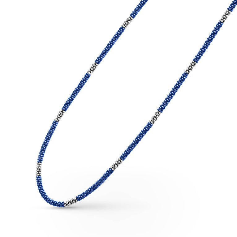 A sterling silver and ceramic beaded necklace angled to the right in the middle of a white background featuring blue ceramic and silver Caviar beading.