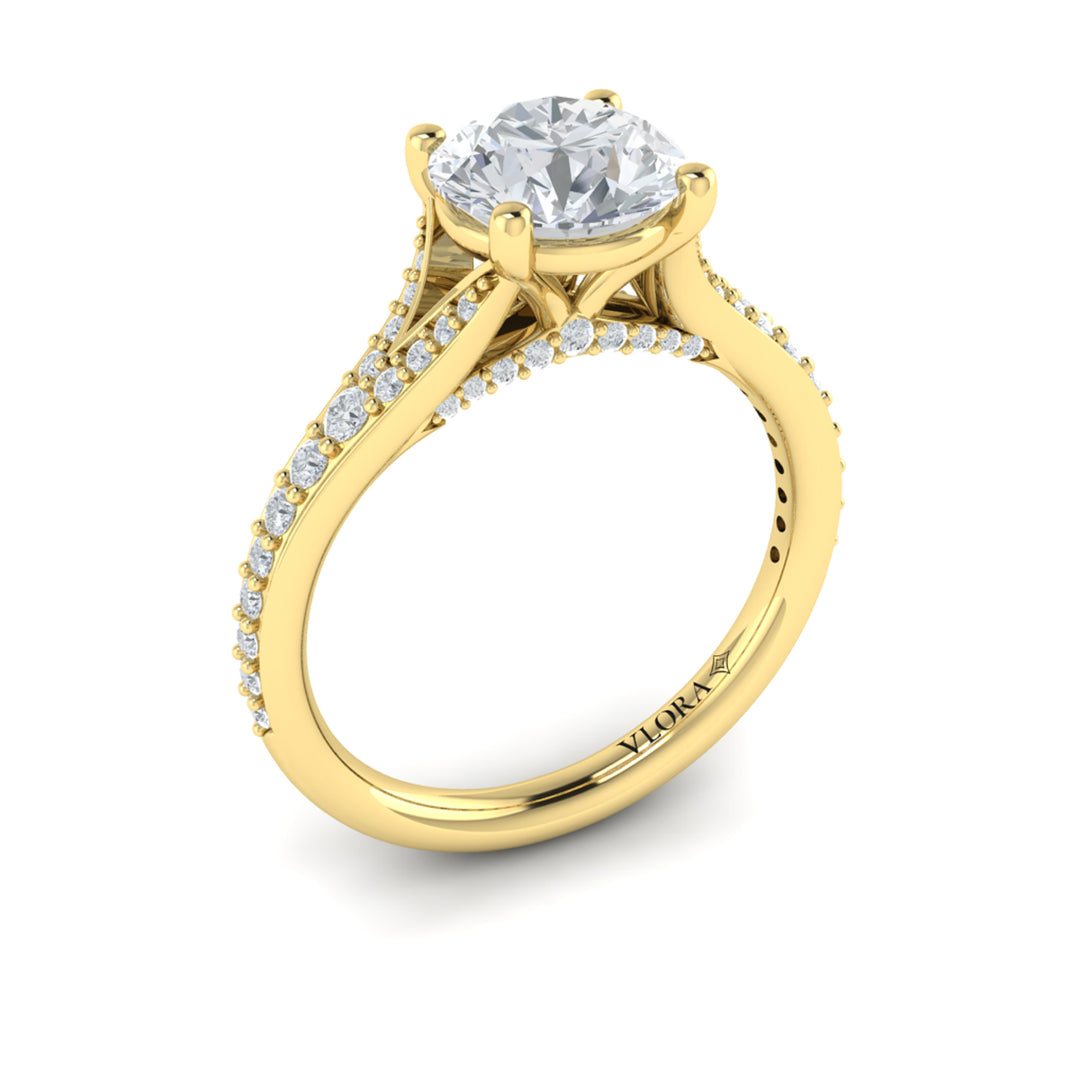 An angled view of a yellow gold engagement ring is set against a white background. The engagement ring features a round center diamond, a split shank design, and a diamond-set band.