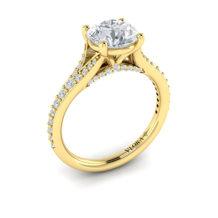 An angled view of a yellow gold engagement ring is set against a white background. The engagement ring features a round center diamond, a split shank design, and a diamond-set band.
