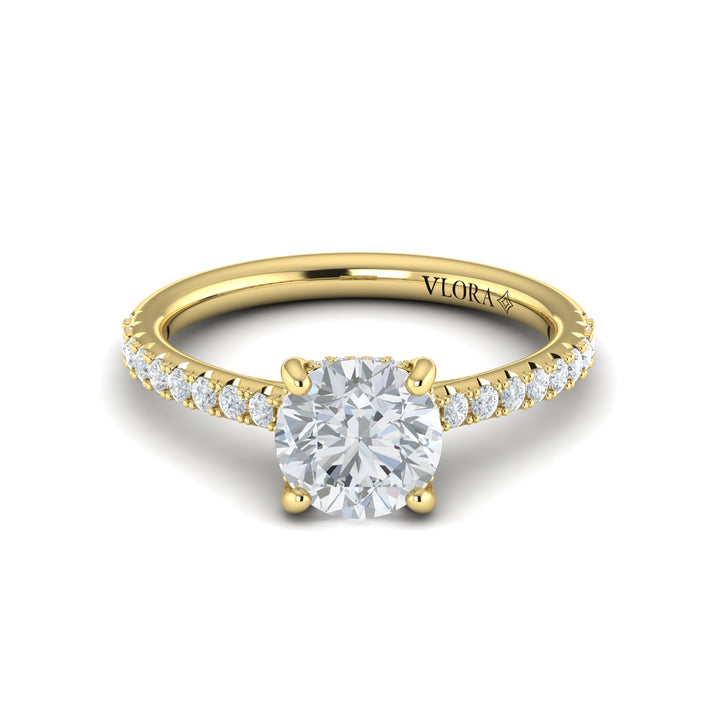 A front view of a yellow gold engagement ring is set against a white background. The engagement ring features a round center diamond, a hidden halo, and a diamond-set band.
