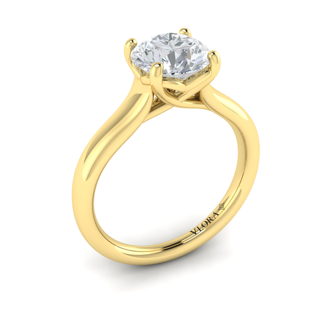An angled view of a yellow gold engagement ring is set against a white background. The engagement ring features a round center diamond, a cathedral setting, and a V-shaped setting.