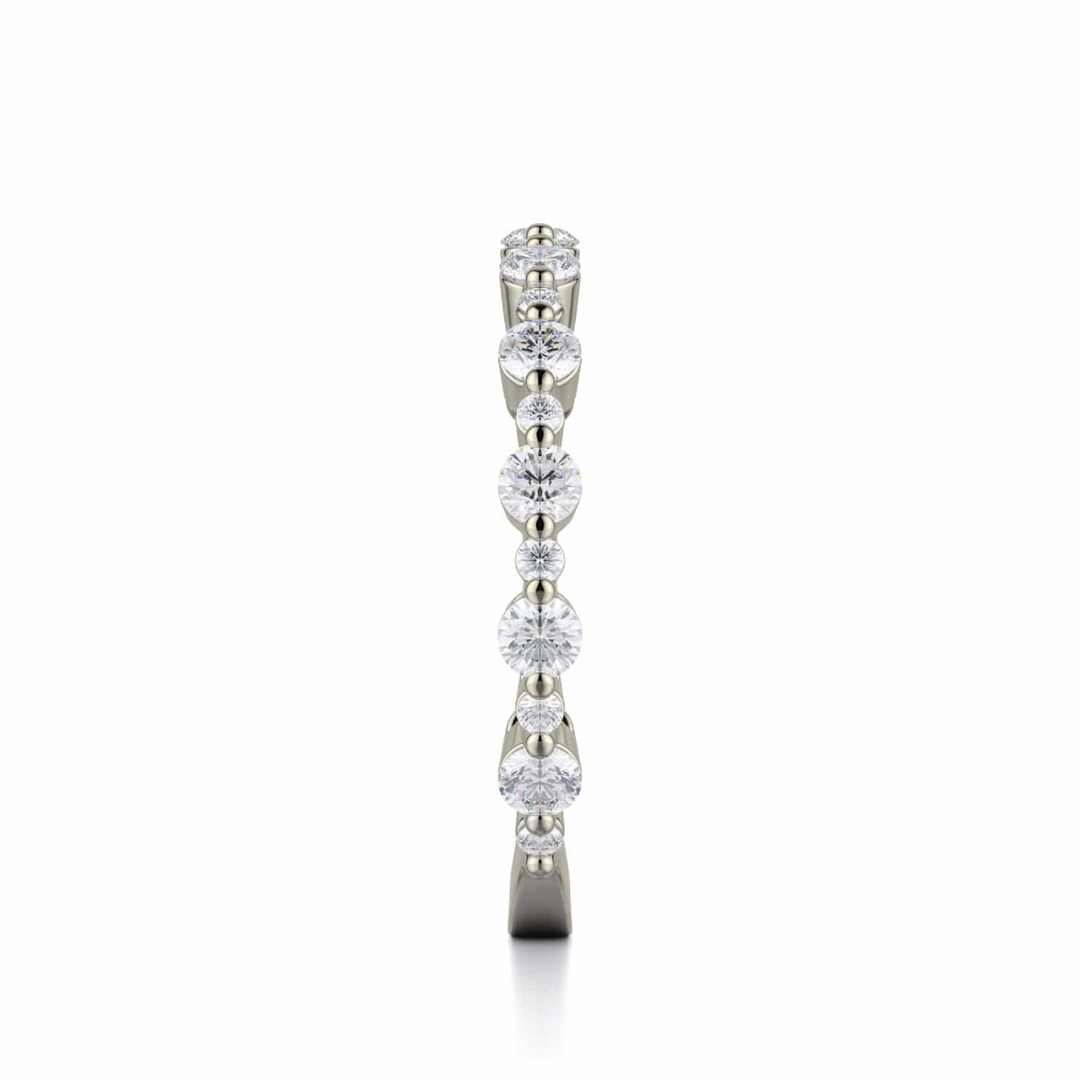A side profile view of a white gold wedding band against a white background. The ring features a 3/4 eternity style with alternating sizes of prong-set round-shaped diamonds.