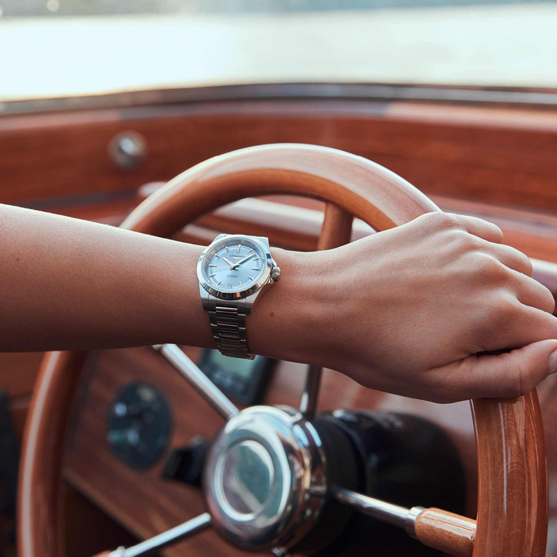 Close up of a woman's arm with her hand on a steering wheel wearing a LONGINES Conquest with a blue dial.