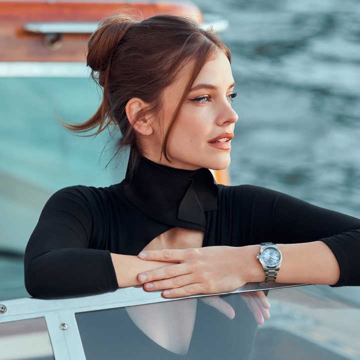 Woman in a black shirt, standing in a boat on the water wearing a LONGINES Conquest with a blue dial.