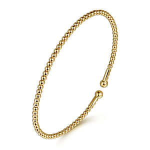 A yellow-gold bangle bracelet with a beaded band and end caps is angled in the middle of a white background.