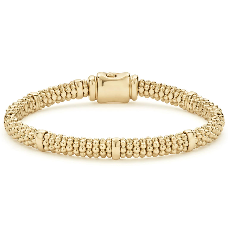 An 18k gold bracelet resting in the middle of a white background. The bracelet features smooth stations, caviar beading, and gold clasp.